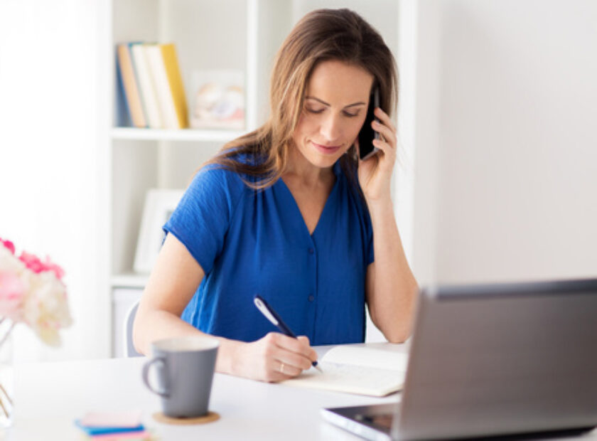 woman with notepad calling on smartphone at office